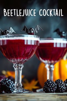 two glasses filled with liquid and topped with blackberries on a table next to pumpkins