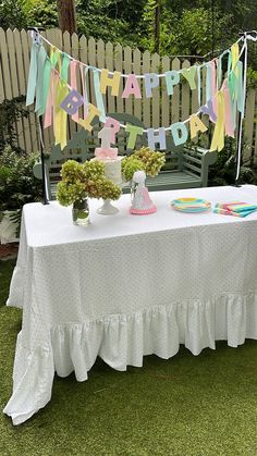 a white table topped with a cake and cupcakes on top of a grass covered field