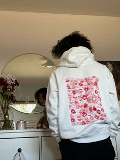 a person standing in front of a mirror wearing a white hoodie with red flowers on it