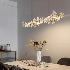 a dining room table with flowers in a vase on it and lights hanging from the ceiling