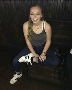 a young woman sitting on top of a wooden bench next to a pair of white shoes