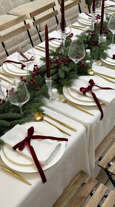 the table is set with white plates, silverware and greenery for christmas dinner