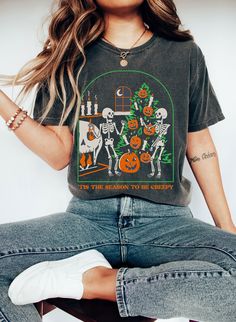 a woman sitting on top of a stool wearing a t - shirt with skeletons and pumpkins