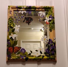 a mirror hanging on the side of a door with flowers and butterflies painted on it