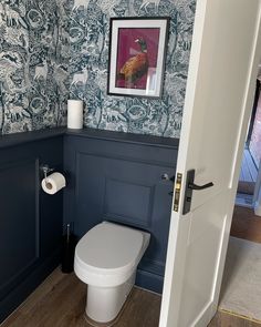 a toilet in a bathroom with blue wallpaper and wooden flooring on the walls