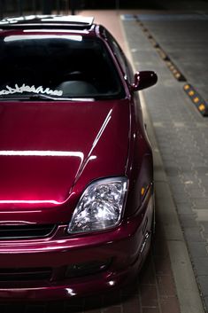 a maroon car is parked on the side of the road with its hood up and it's lights turned on