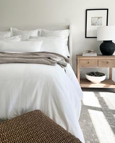 a bed with white linens and pillows in a small room next to a table