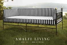 a black and white striped couch sitting on top of a green grass covered field with trees in the background