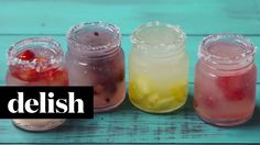 four jars filled with different types of drinks on top of a blue wooden table and the words delish above them