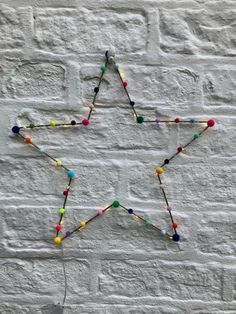 a star made out of beads on a white brick wall with a string attached to it