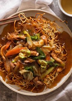 a bowl filled with noodles and vegetables next to chopsticks on top of a table