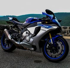 a blue and silver motorcycle parked next to a stone wall