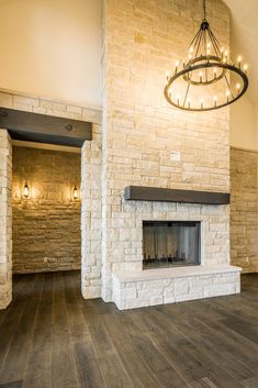 an empty living room with a fireplace and chandelier hanging from it's ceiling