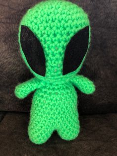 a crocheted green alien doll sitting on a brown couch with its eyes closed