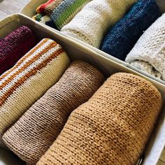 a box filled with lots of different colored knitted pillows on top of a wooden floor