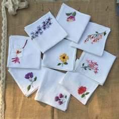 six embroidered napkins with flowers on them sitting on top of a piece of cloth