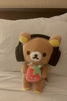 a brown teddy bear sitting on top of a bed with headphones around its neck