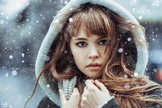 a young woman is standing in the snow wearing a hoodie and looking at the camera