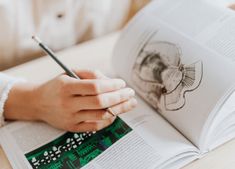 a person sitting at a table with an open book and a pencil in their hand