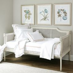 a bed with white sheets and pillows in a room next to pictures on the wall