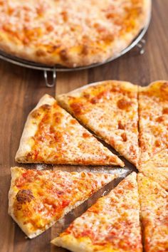 sliced pizza sitting on top of a wooden table next to a pan with one slice missing