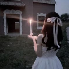 a woman holding a lit candle in front of a house