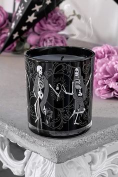 a black candle with skeletons on it sitting on a table next to some pink flowers