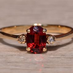 a close up of a ring with a red stone in the middle and two diamonds on each side