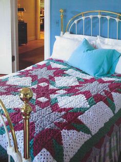 a bed with a crocheted blanket on top of it next to a blue wall