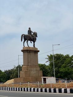 a statue of a man riding a horse on top of a cement pillar with trees in the background