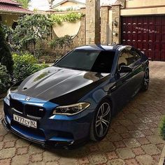 a blue bmw is parked in front of a brick driveway with a red garage door