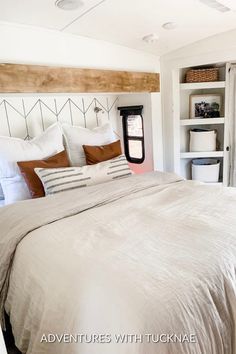 a bed with white sheets and brown pillows in a bedroom next to a book shelf