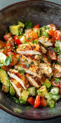 a bowl filled with chicken, cucumber and tomatoes