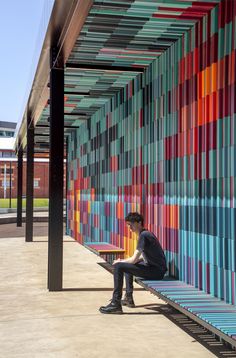 a person sitting on a bench in front of a colorful wall