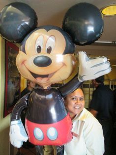 a woman standing next to a giant mickey mouse balloon