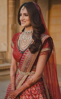 a woman in a red and gold bridal outfit with her hands on her hips