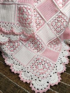 a pink and white crocheted blanket sitting on top of a wooden floor next to a pillow