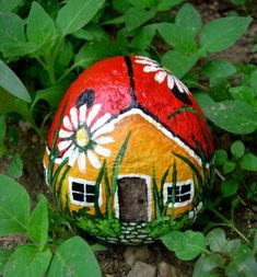 a painted rock sitting in the grass with flowers on it's face and an orange house