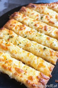 cheesy bread sticks are lined up on a black plate and ready to be eaten