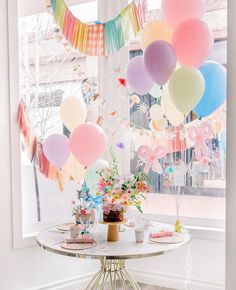 a table topped with lots of balloons and confetti on top of it next to a window