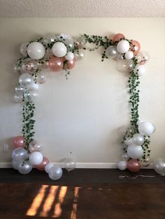 an arch made out of balloons and greenery is displayed in front of a wall