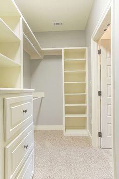 an empty walk in closet with white shelves and drawers on either side of the closet door