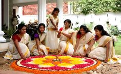 a group of women sitting around a flower arrangement on the ground in front of a building