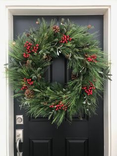 a christmas wreath hanging on the front door with holly and red berries, pine cones and evergreen needles