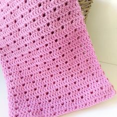 a pink crocheted blanket sitting on top of a white table next to a basket