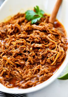 a white bowl filled with shredded meat and garnished with cilantro leaves