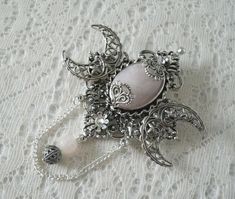 Rose Quartz Triple Moon Brooch This beautiful silver plated brooch has silver plated crescent moons, silver plated embellishments, a rose quartz setting, rhinestone, metal chain, silver plated filigree bead and rose quartz bead. Can also be worn as a cloak pin. It is 2.75 inches wide and 3.75 inches long with bead drop and chain. Gothic Brooch Jewelry Gift, Silver Bohemian Brooch Jewelry, Silver Bohemian Jewelry Brooch, Handmade Silver Bohemian Brooch, Spiritual Silver Brooch, Spiritual Silver Jewelry Brooch, Spiritual Silver Brooch For Gift, Cloak Pin, Embossed Leather Journal