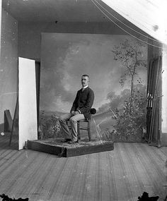 an old photo of a man sitting on a chair in front of a wall painting