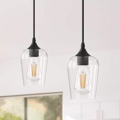 two clear glass pendant lights hanging from a ceiling fixture in a kitchen area with white cabinets and countertops