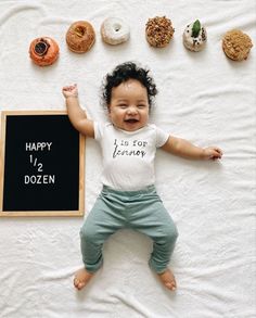 a baby laying on top of a bed next to doughnuts and a chalkboard